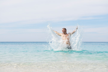 Bright sunny view of young man leaping out of tropical blue waters with an outstretched splash