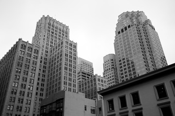 Fototapeta na wymiar Bleak monochrome city skyline featuring traditional brick towers and modern glass and steel skyscrapers with smaller buildings in the foreground