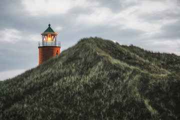 Fototapeta na wymiar Lit lighthouse on a hill with tall grass and moss on Sylt island