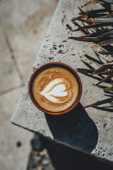 Heart latte coffee art in ceramic cup on a marble tile outdoors.