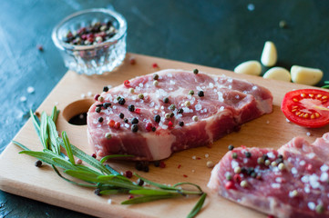 Raw pork meat sprinkled with pepper and salt with chopped tomato garlic and rosemary, steak cooking process