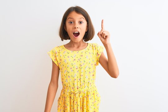 Young Beautiful Child Girl Wearing Yellow Floral Dress Standing Over Isolated White Background Pointing Finger Up With Successful Idea. Exited And Happy. Number One.