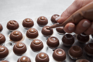 Cooking handmade chocolates. A confectioner pours liquid  chocolate into molds. Close-up. Selective focus.