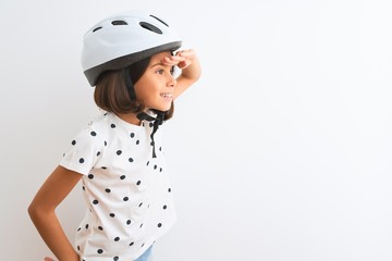 Beautiful child girl wearing security bike helmet standing over isolated white background very happy and smiling looking far away with hand over head. Searching concept.