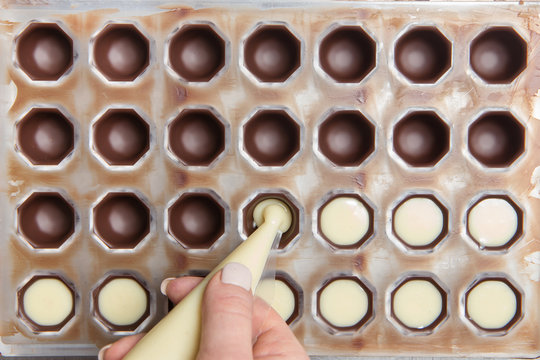 Production Of Chocolates. Chocolatier Is Pouring Melted White Chocolate Mass Into Molds. Chocolate Factory.