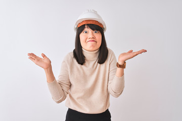 Young beautiful Chinese architect woman wearing helmet over isolated white background clueless and...