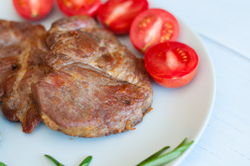 Tasty, juicy, fried meat steaks of pork or beef with sauce, spices and tomato on gray plate, on a light wooden background, top view