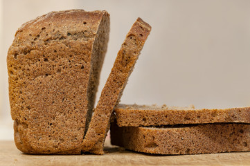 Half of rye brown bread with some bread slices on a chopping board.