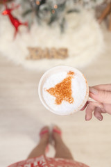 Female holding cappuccino with Christmas tree design on froth