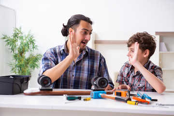 Young father repairing skateboard with his son at home
