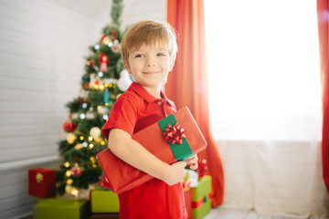 Obraz na płótnie Canvas Cute little boy of about five year with a gift in a decorated Christmas room with a xmas tree.