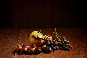 Autumn fruit composition with pommegranate, black grapes and chestnuts on a wooden table