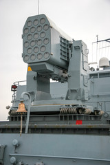 Multi-barrel missile launcher on a NATO ship. Many gun barrels. An interesting system of depreciation from steel cables. Near the ship's bell.