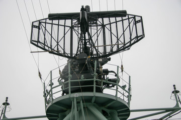 Radar on a NATO warship with a circular platform for people. A lot of wires and parts. Rainy gloomy...
