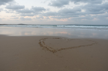 Heart drawn in the sand with people surfing in the background