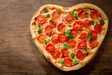 Valentines Day food. Heart shapped pepperoni pizza with green basil,  top view