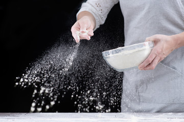 Professional cook in a kitchen sprinkles flour on the table to make dough