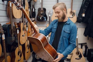 Wall murals Music store Bearded young man choosing a guitar in music store