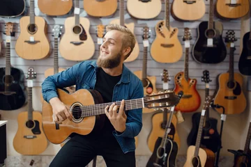 Foto op Plexiglas Muziekwinkel Young man plays on acoustic guitar in music store