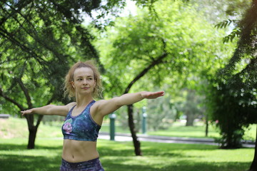 Fototapeta premium Girl with curly blond hair doing yoga outdoors in the park.