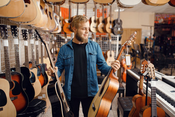 Young guy choosing acoustic guitar in music store