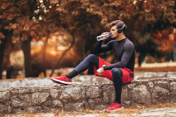 Portrait of  young man on a morning jogging in the autumn park, man listening to music with headphones