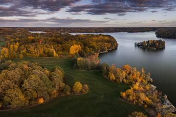 Naklejka premium Aerial view of orange and yellow autumn trees and green fields around a lake