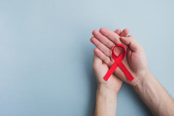 Man hands hold red ribbon awareness Aids on a light blue background. Medicine concept, World Aids...