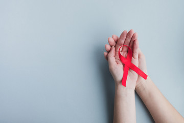 Womans hands hold red ribbon awareness Aids on a light blue background. Medicine concept, World...