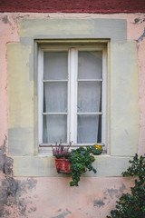 Fototapeta na wymiar Old, rustic building exterior. Window with flowers on a bright pink wall. Travel, architecture concept