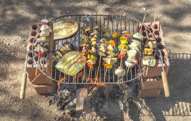 Rustic vegan barbecue made with recycled bricks. Cooking skewers and vegetables on the fire during...