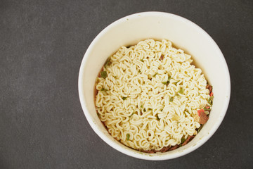 Hand uses chopsticks to pickup tasty noodles with steam and smoke in bowl on wooden background, selective focus. Asian meal on a table, junk food concept