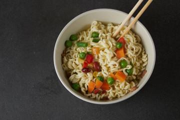 Hand uses chopsticks to pickup tasty noodles with steam and smoke in bowl on wooden background, selective focus. Asian meal on a table, junk food concept
