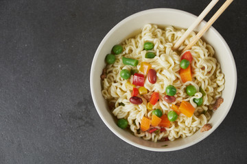 Hand uses chopsticks to pickup tasty noodles with steam and smoke in bowl on wooden background,...