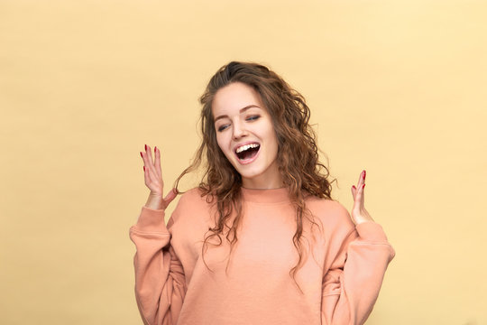 Portrait of a young beautiful woman wearing sweatshirt holding hands in front of her isolated over yellow background