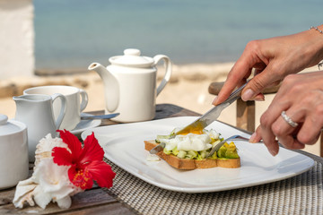 Healthy sandwich with avocado, cucumber and poached eggs on table for healthy breakfast on the beach near sea. Food and breakfast concept.