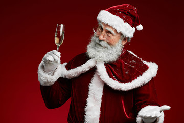Waist up portrait of Santa Claus holding champagne glass while standing over red background, copy...