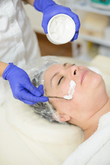 Young female cosmetologist applies cosmetic product on the face of female patient. Spa, cosmetic procedure