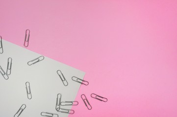 A group of silver paper clip on the white paper on the pink background