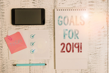 Writing note showing Goals For 2019. Business concept for object of demonstratings ambition or effort aim or desired result Square spiral notebook marker smartphone sticky note on wood background
