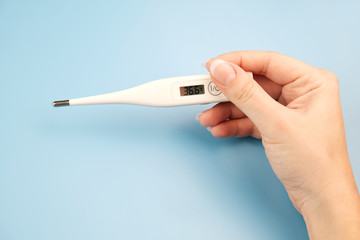 Female hand holding a digital thermometer on blue background. Healthy Temperature 36.6.
