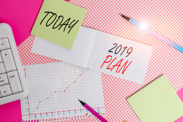 Writing note showing 2019 Plan. Business concept for setting up your goals and plans for the current year or in 2019 Writing equipments and computer stuffs placed above colored plain table