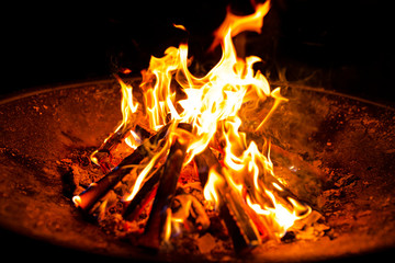 High flames from a burning wood fire on a metal grate at night.