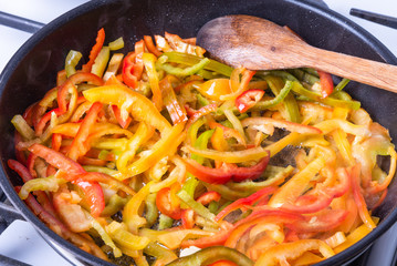 Sliced sweet pepper is fried in a pan and stirred with a wooden spoon - cooking sauce