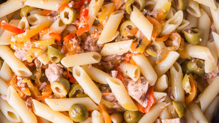 Italian cuisine - penne rigate pasta with tuna, olives and pepper sauce cooked in a pan, close-up
