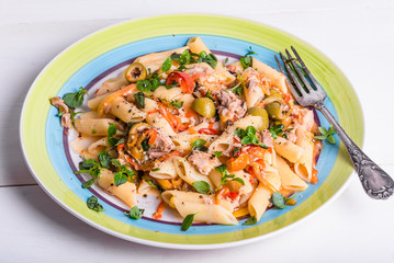 Italian cuisine - penne rigate pasta with sweet pepper sauce with tomatoes, tuna with olives on a plate on a light wooden table
