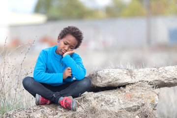 Bored child sitting on a rock in the countryside - obrazy, fototapety, plakaty