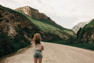 Naklejka premium fashionable girl in white clothes standing on the road in the highlands . green grass and mountains