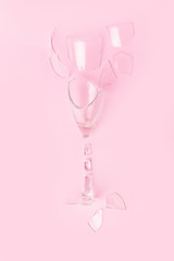 a glass of champagne is broken into pieces on a trendy pastel pink background. Flat lay style.
