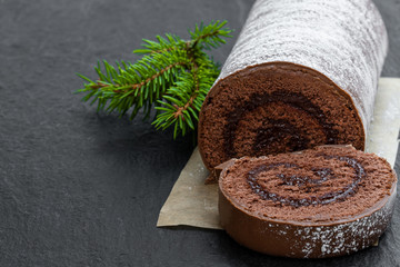 Chocolate yule log christmas cake coated with milk chocolate on black stone background